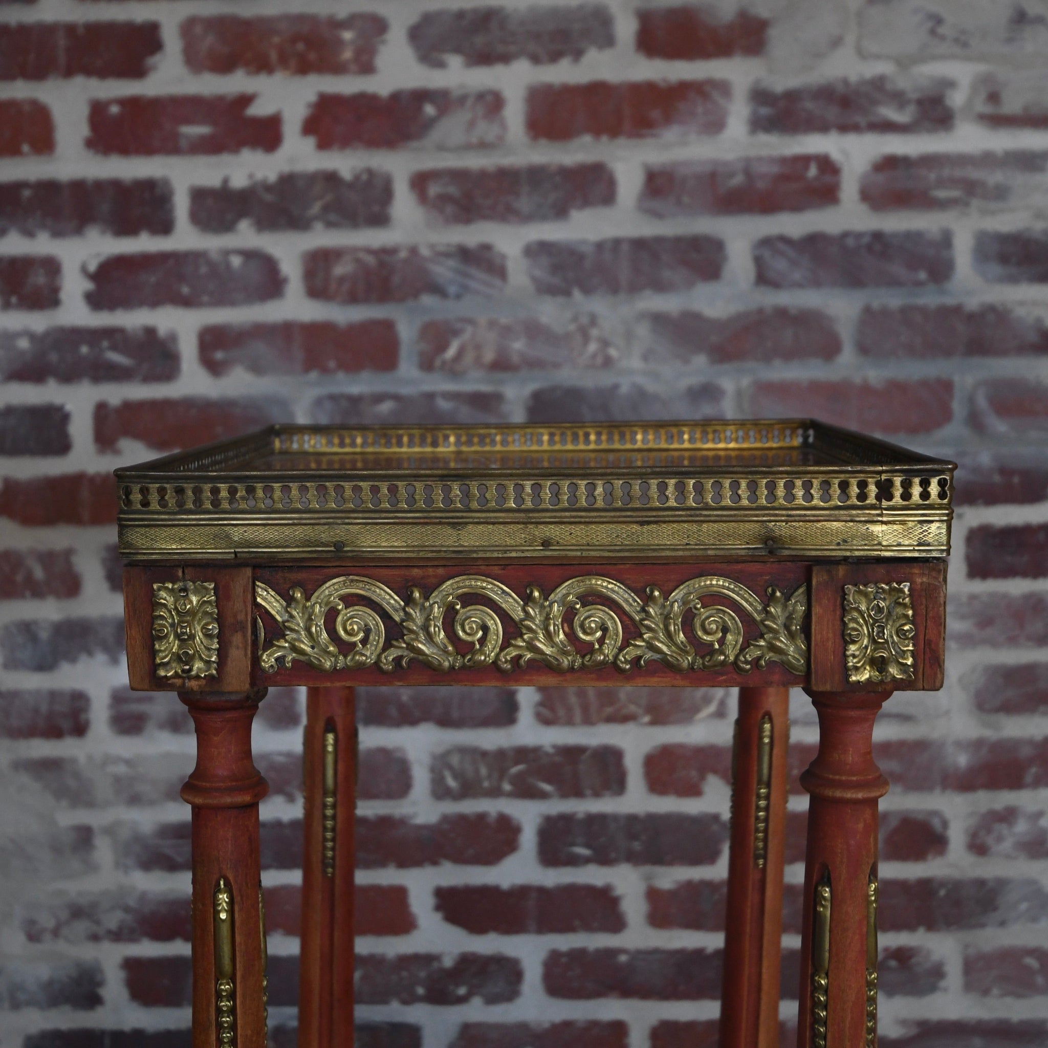 Decorative wooden table with gold embellishments against a brick wall.