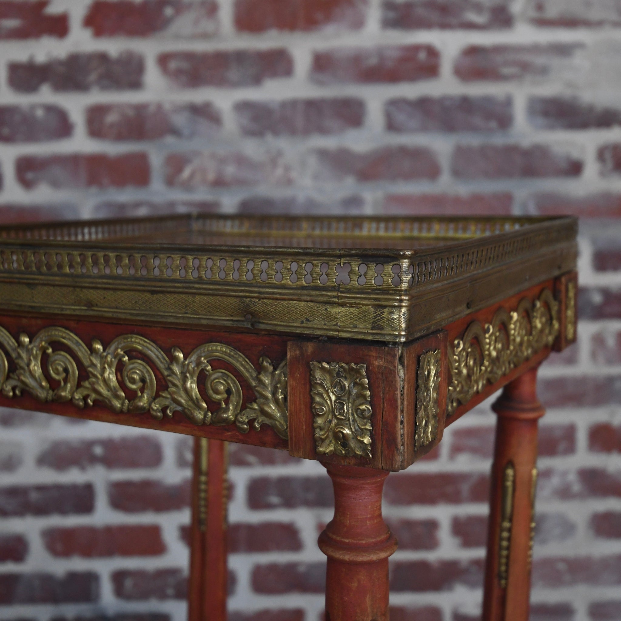 Decorative wooden table with gold embellishments against a brick wall.
