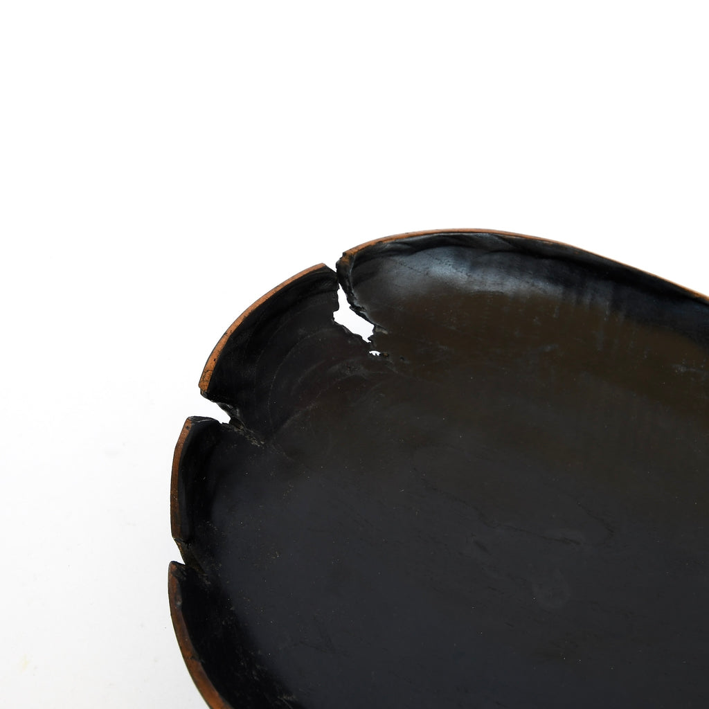 A close-up of a cracked black ceramic plate against a white background, beside a hand-made wooden Golden Oldies bowl.