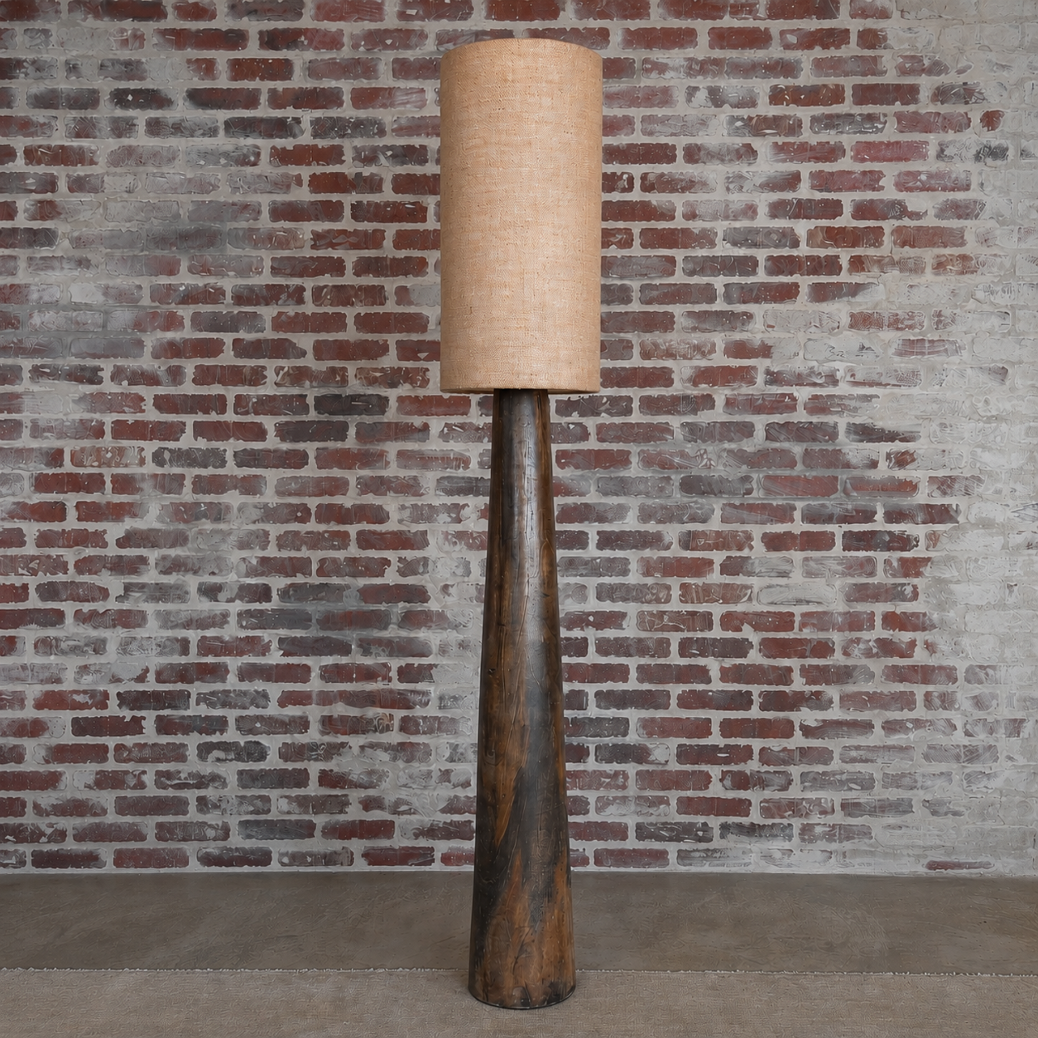 Floor lamp with a textured beige shade against a brick wall.