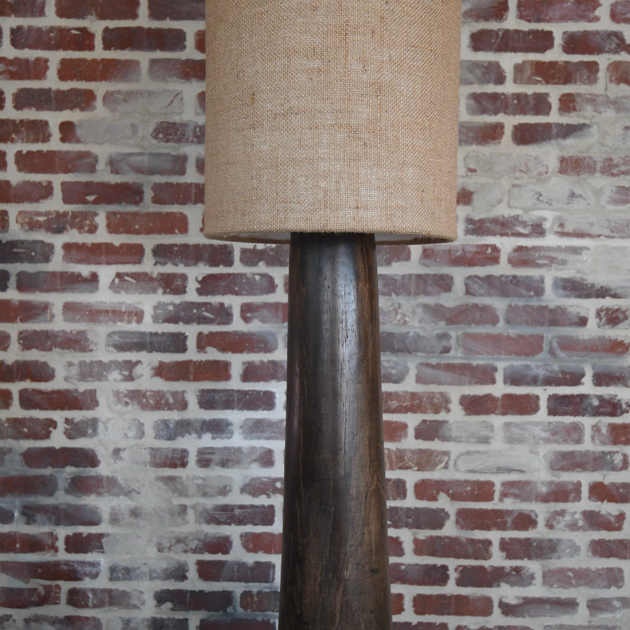 Floor lamp with a beige lampshade against a brick wall