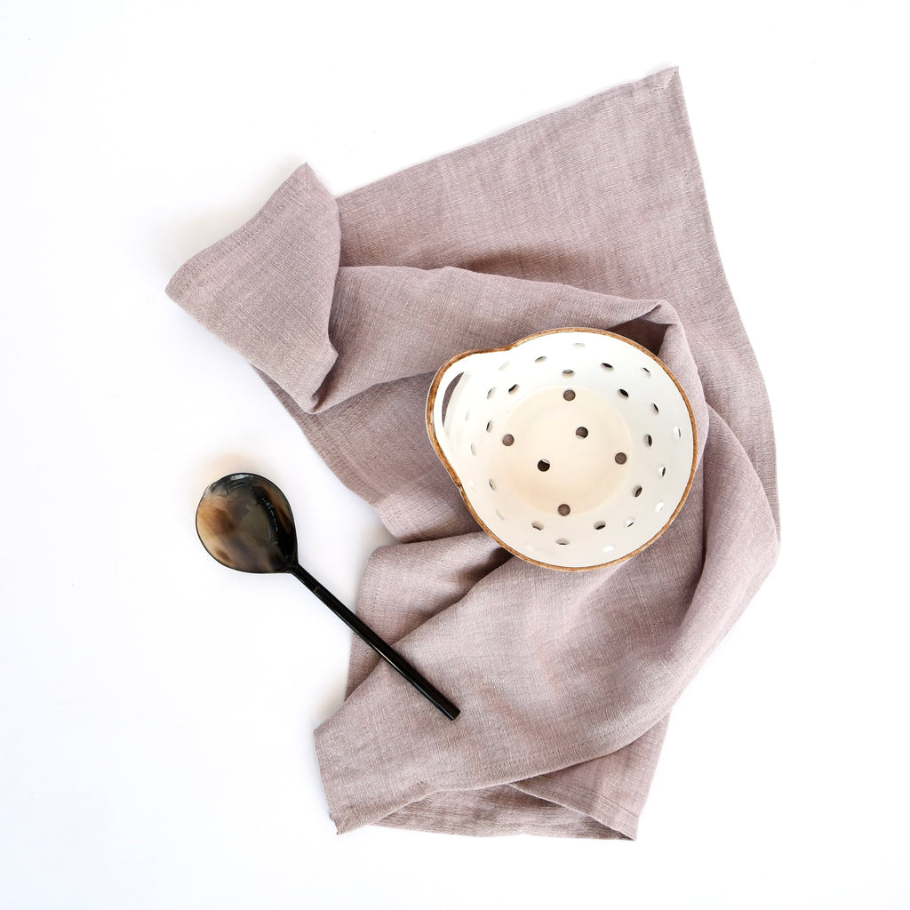 A white bowl with holes and a black spoon on Kitchen Elegance Lilac Tea Towels Set against a white background.