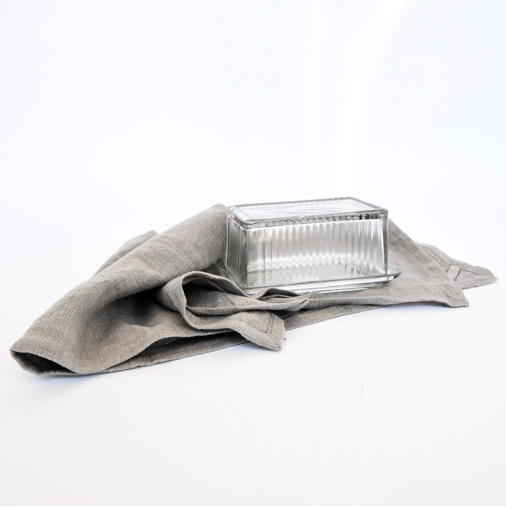 Empty glass loaf pan on a Linen Tales Gray Linen Tea Towels Set against a white background.