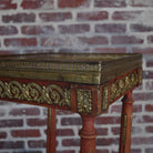 Decorative wooden table with gold embellishments against a brick wall.